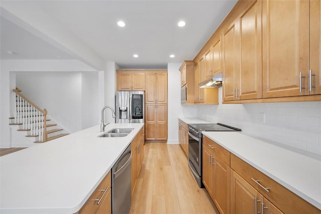 kitchen with appliances with stainless steel finishes, sink, decorative backsplash, a kitchen island with sink, and light wood-type flooring