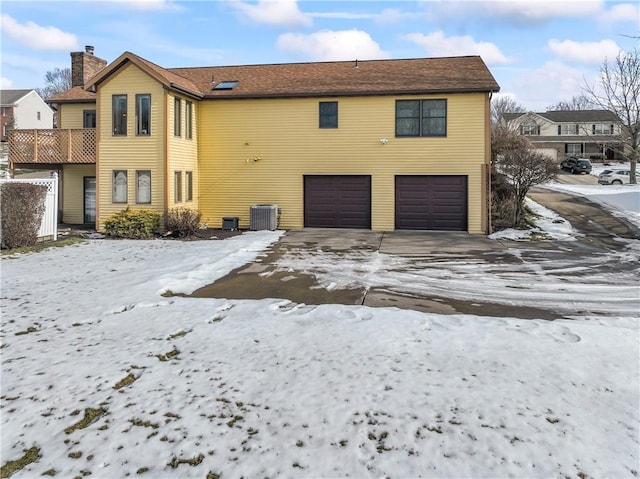 snow covered house with a garage and central AC unit