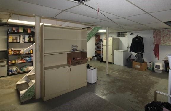 basement with white fridge, a drop ceiling, and refrigerator