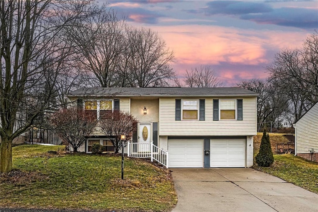 raised ranch with an attached garage, concrete driveway, and a yard