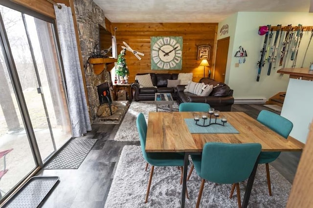 dining area with a baseboard heating unit, dark wood-type flooring, a fireplace, and wooden walls