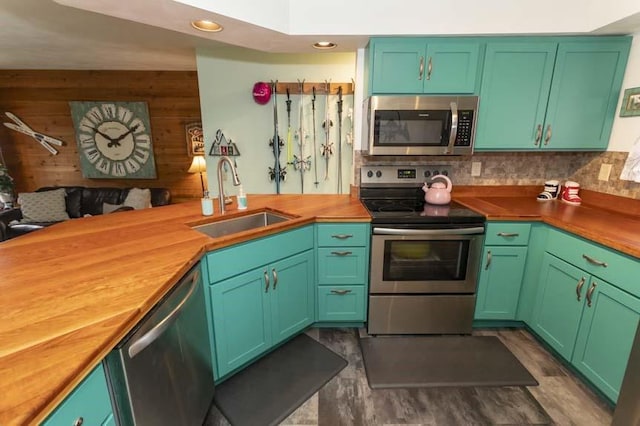 kitchen with appliances with stainless steel finishes, wood counters, wood walls, sink, and green cabinets