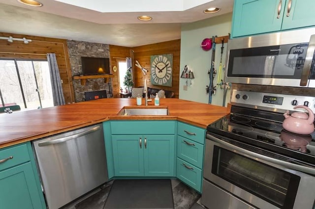 kitchen featuring butcher block countertops, a stone fireplace, stainless steel appliances, and sink