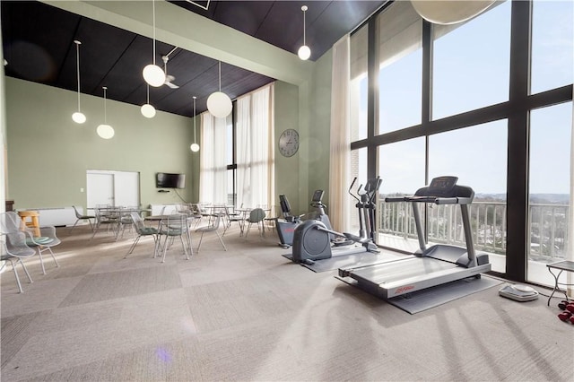 exercise room featuring expansive windows, carpet, and a towering ceiling