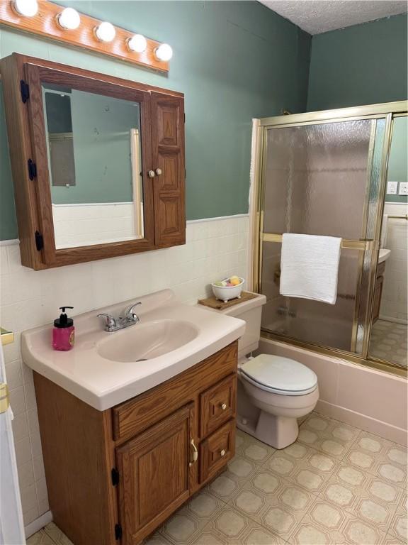 full bathroom with shower / bath combination with glass door, tile walls, vanity, a textured ceiling, and toilet