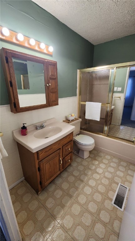 full bathroom with toilet, shower / bath combination with glass door, tile walls, a textured ceiling, and vanity