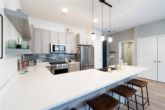 kitchen with a kitchen bar, sink, hanging light fixtures, and appliances with stainless steel finishes