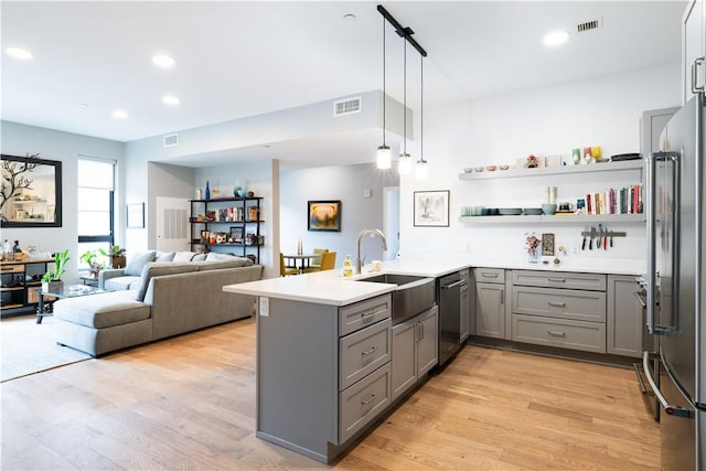 kitchen with sink, light hardwood / wood-style flooring, kitchen peninsula, pendant lighting, and stainless steel appliances