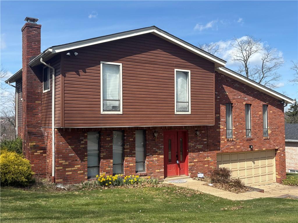 view of front of house featuring a front lawn, a chimney, a garage, and brick siding