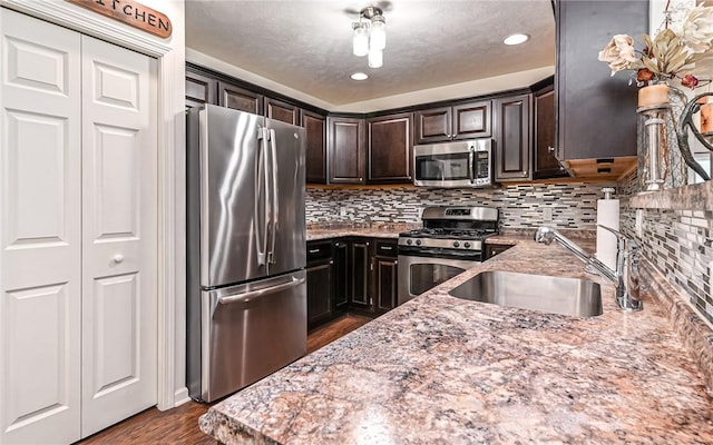 kitchen featuring sink, backsplash, light stone counters, dark brown cabinetry, and stainless steel appliances