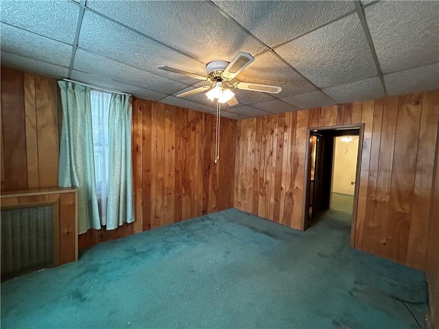 interior space featuring carpet, a paneled ceiling, ceiling fan, and wood walls