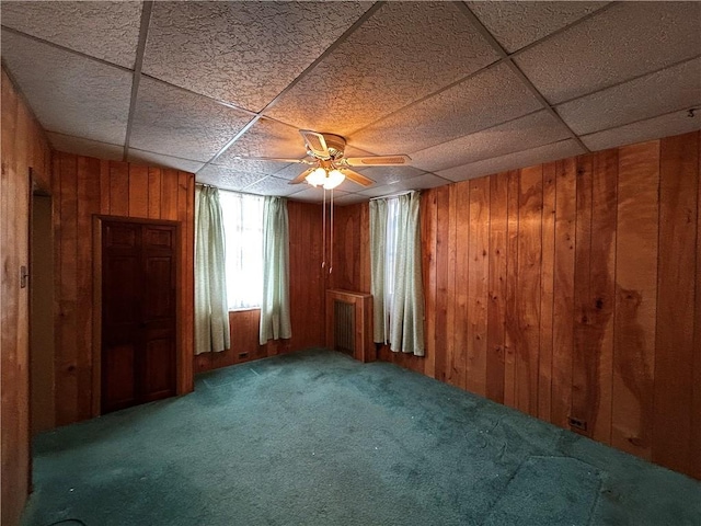 carpeted spare room featuring a paneled ceiling and wooden walls