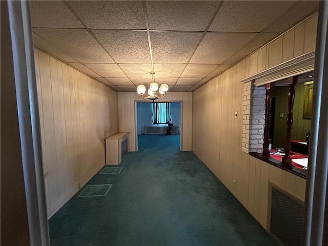 hallway with an inviting chandelier, carpet, a paneled ceiling, and wooden walls