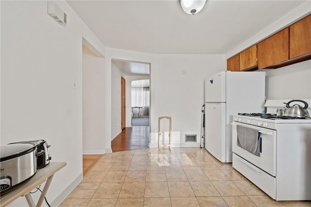 kitchen featuring visible vents, baseboards, gas range gas stove, light tile patterned floors, and brown cabinets