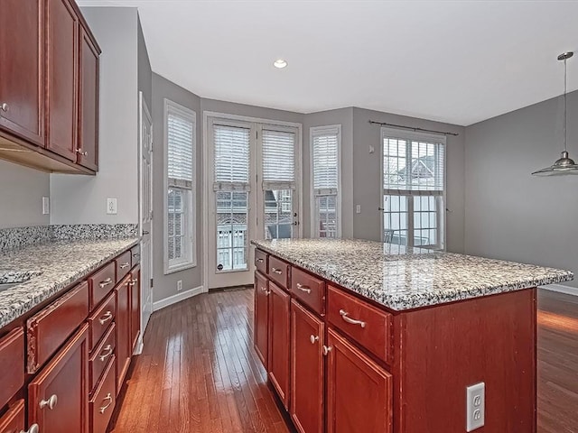 kitchen featuring dark hardwood / wood-style flooring, decorative light fixtures, light stone countertops, and a kitchen island