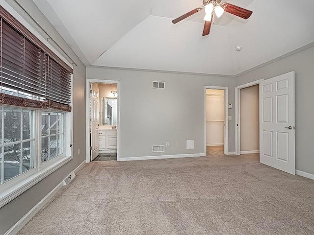 unfurnished bedroom with lofted ceiling, connected bathroom, a spacious closet, ceiling fan, and carpet