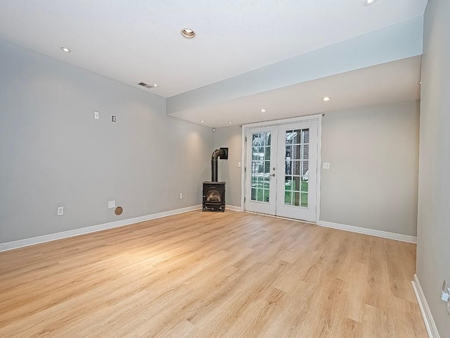 unfurnished living room with french doors, light hardwood / wood-style floors, and a wood stove