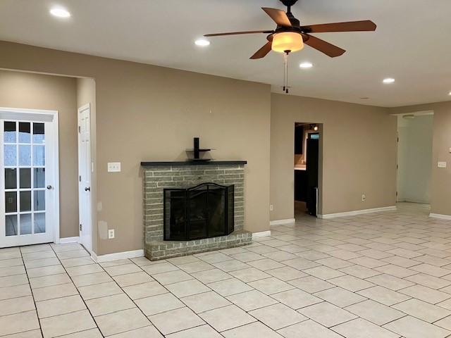 unfurnished living room with light tile patterned flooring, ceiling fan, and a brick fireplace