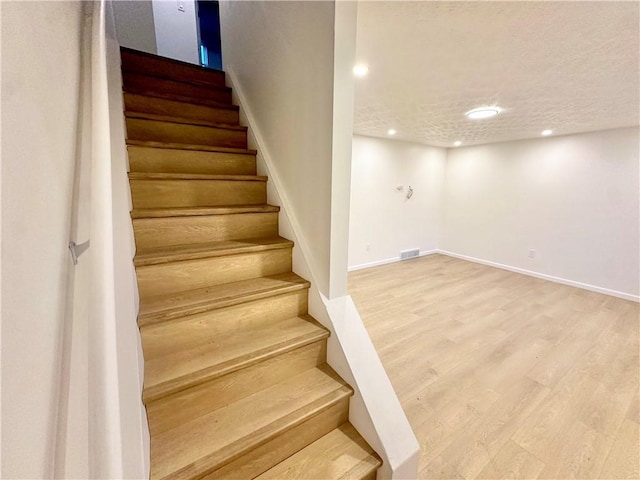 stairs with wood-type flooring and a textured ceiling