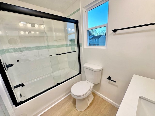 full bathroom with hardwood / wood-style flooring, bath / shower combo with glass door, sink, and toilet