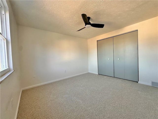 unfurnished bedroom with ceiling fan, light colored carpet, a closet, and a textured ceiling