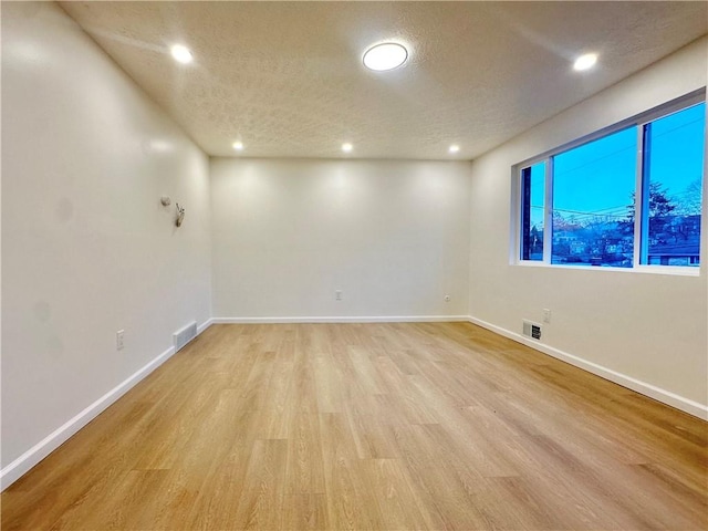 spare room with a textured ceiling and light wood-type flooring