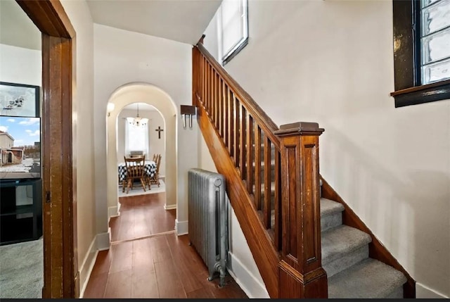 staircase featuring arched walkways, hardwood / wood-style floors, baseboards, and radiator