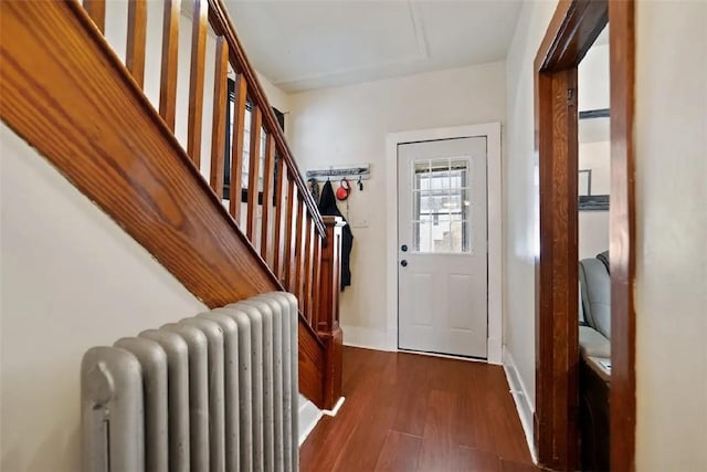 doorway to outside featuring dark wood-style floors, radiator heating unit, stairway, and baseboards