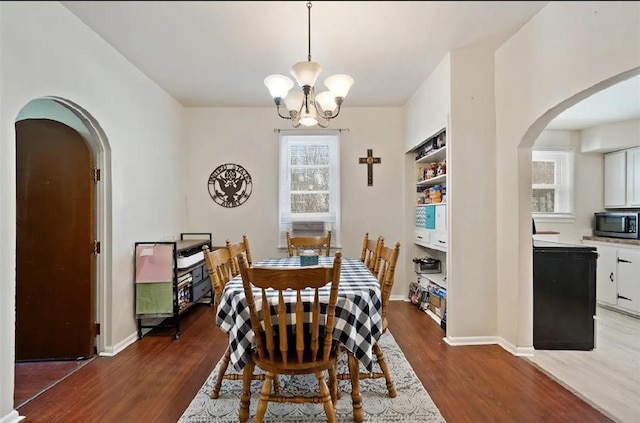 dining space featuring a wealth of natural light, arched walkways, dark wood finished floors, and a notable chandelier