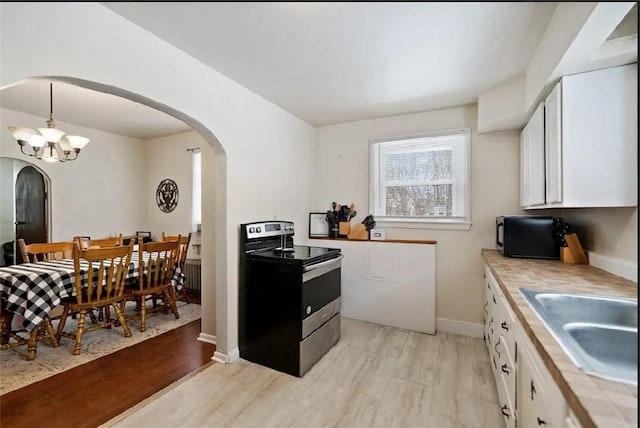 kitchen featuring arched walkways, white cabinetry, a sink, black microwave, and stainless steel electric range