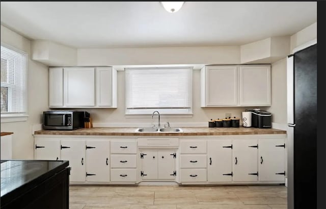 kitchen with light countertops, stainless steel microwave, freestanding refrigerator, white cabinetry, and a sink