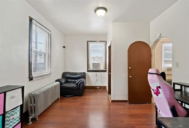 home office with baseboards, radiator heating unit, arched walkways, and wood finished floors