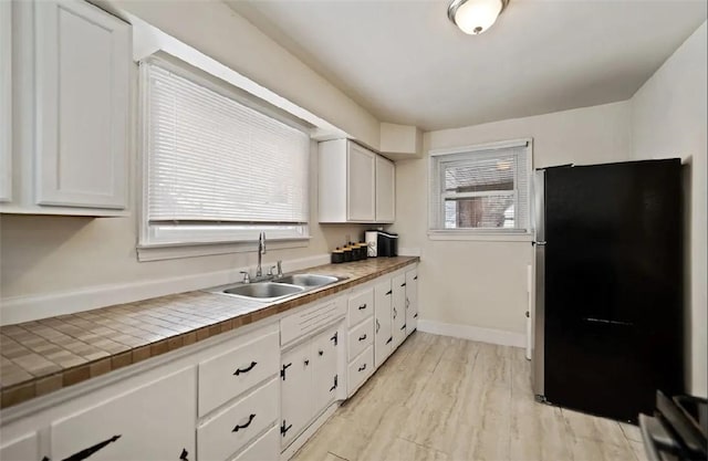 kitchen with baseboards, white cabinets, freestanding refrigerator, light wood-type flooring, and a sink