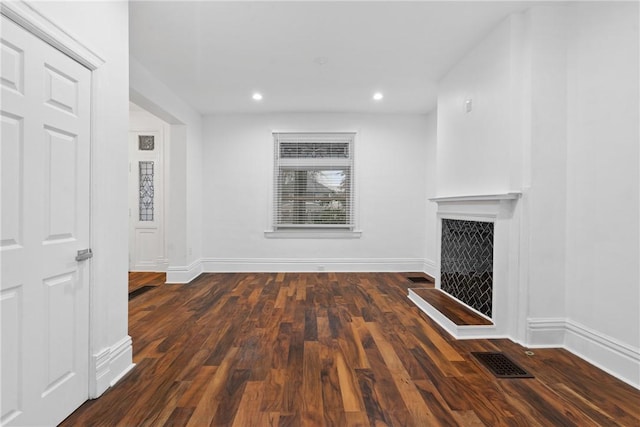 unfurnished living room featuring a fireplace with raised hearth, recessed lighting, dark wood-style flooring, visible vents, and baseboards