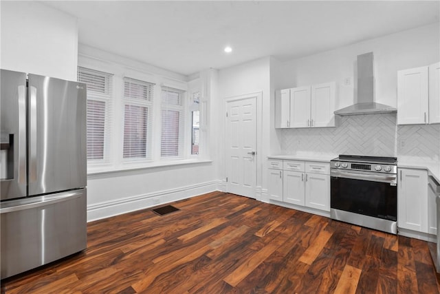 kitchen with wall chimney range hood, appliances with stainless steel finishes, white cabinetry, tasteful backsplash, and dark hardwood / wood-style flooring