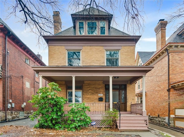 american foursquare style home with covered porch, brick siding, and a chimney