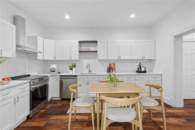 kitchen featuring wall chimney exhaust hood, stainless steel appliances, light countertops, white cabinetry, and a sink