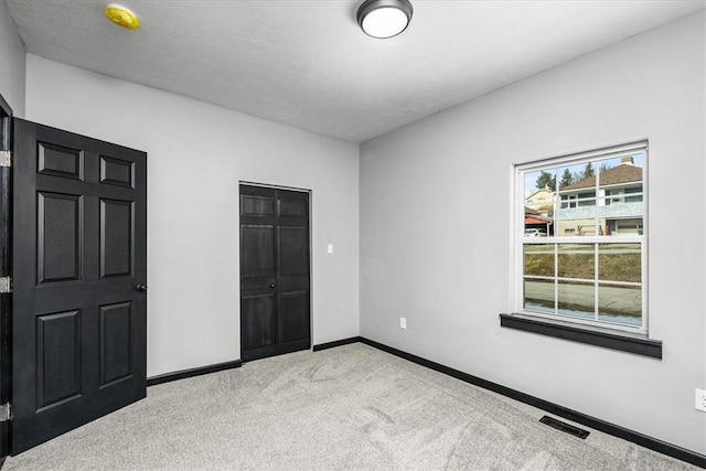 unfurnished bedroom featuring light colored carpet, a textured ceiling, and a closet