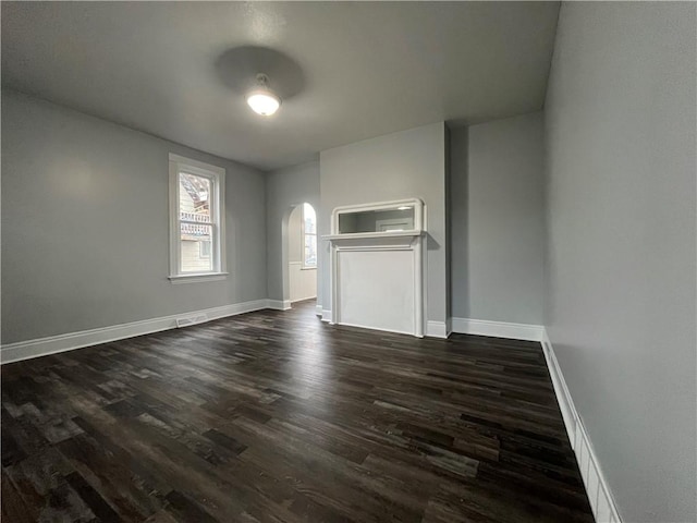 unfurnished living room featuring arched walkways, visible vents, baseboards, and dark wood finished floors