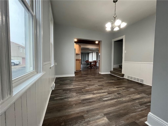 unfurnished dining area with dark wood finished floors, visible vents, an inviting chandelier, and stairs