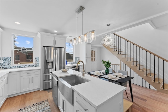 kitchen with sink, white cabinetry, a kitchen island with sink, stainless steel fridge with ice dispenser, and decorative light fixtures