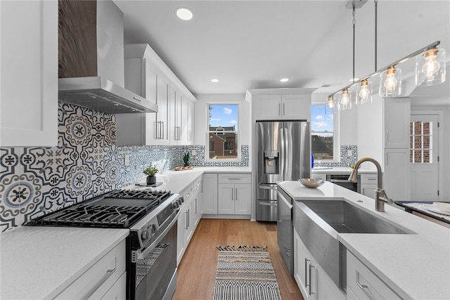 kitchen with appliances with stainless steel finishes, sink, white cabinets, hanging light fixtures, and wall chimney exhaust hood