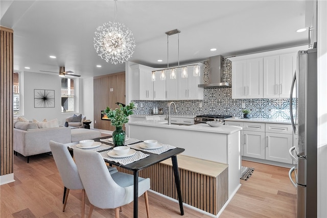 kitchen featuring appliances with stainless steel finishes, pendant lighting, white cabinetry, light hardwood / wood-style floors, and wall chimney range hood