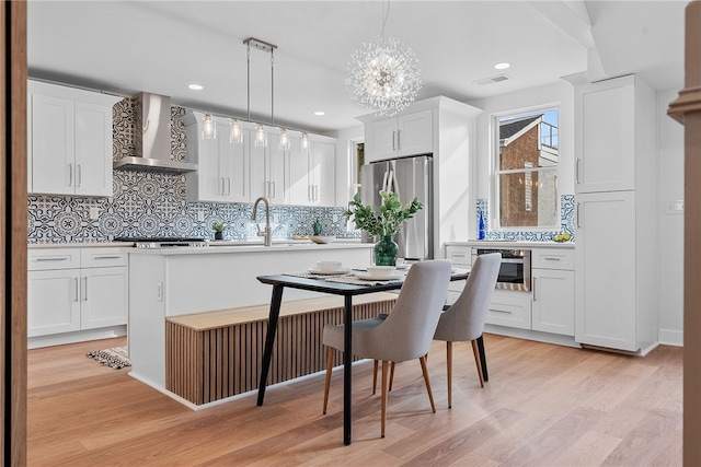 kitchen featuring a kitchen island, appliances with stainless steel finishes, decorative light fixtures, white cabinets, and wall chimney exhaust hood