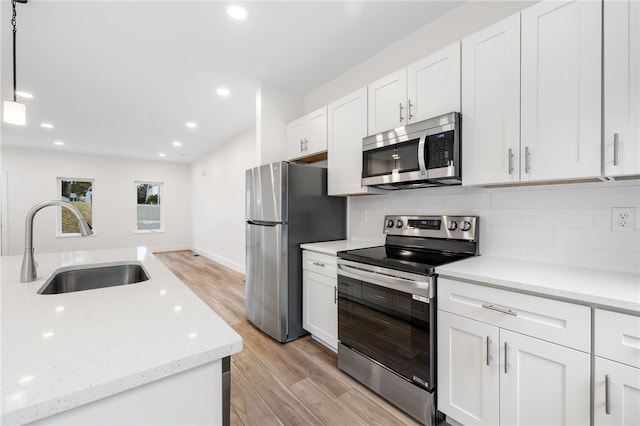 kitchen with sink, light stone counters, decorative light fixtures, stainless steel appliances, and white cabinets