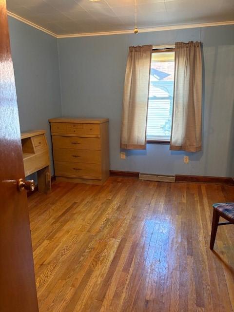 unfurnished bedroom with a baseboard heating unit, hardwood / wood-style flooring, and ornamental molding