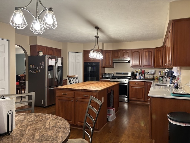 kitchen featuring dark wood-type flooring, wood counters, decorative light fixtures, a center island, and stainless steel appliances