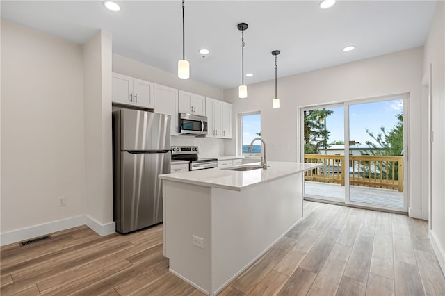 kitchen with sink, light hardwood / wood-style flooring, appliances with stainless steel finishes, white cabinetry, and a kitchen island with sink