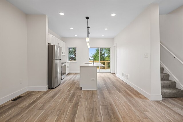 kitchen featuring white cabinetry, stainless steel refrigerator, pendant lighting, a kitchen island with sink, and stove
