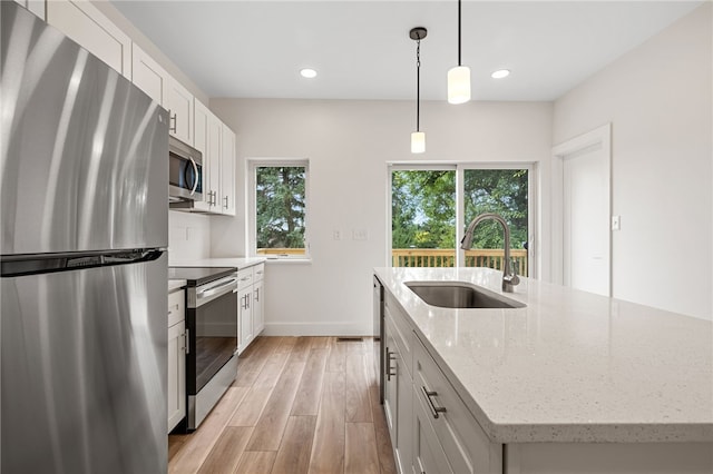 kitchen featuring sink, white cabinetry, appliances with stainless steel finishes, light stone countertops, and a kitchen island with sink